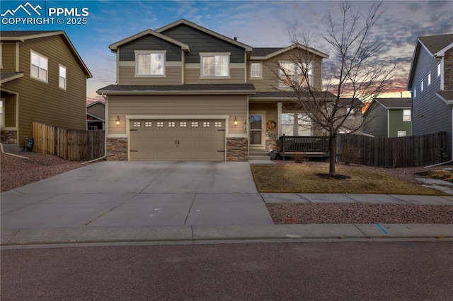 view of front of house featuring driveway, stone siding, and fence