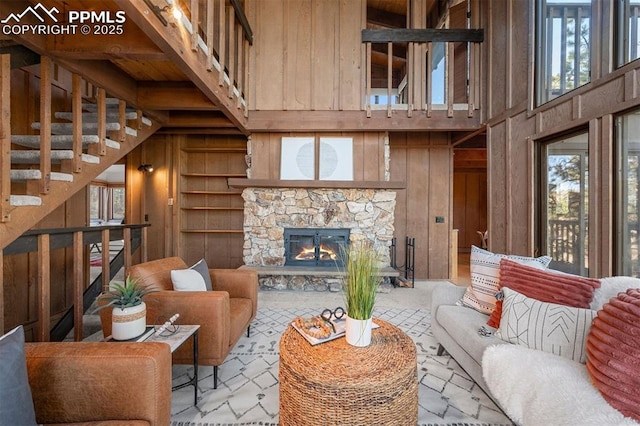 living area with a stone fireplace, wooden walls, a towering ceiling, and stairs