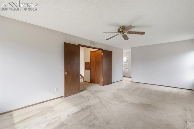 spare room with light carpet, ceiling fan, visible vents, and a textured ceiling