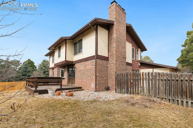 view of side of property with brick siding, fence, a wooden deck, stucco siding, and a chimney