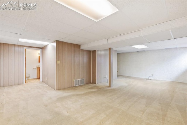 finished basement featuring a drop ceiling, carpet, visible vents, and wooden walls