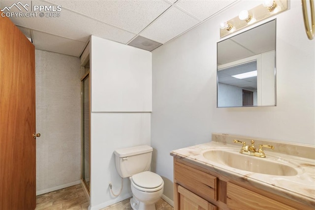 full bath with a drop ceiling, toilet, vanity, baseboards, and a shower with door