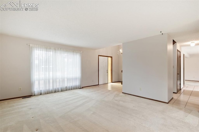 spare room with light carpet, a notable chandelier, and baseboards