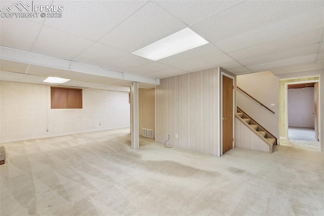 finished below grade area featuring carpet floors, a paneled ceiling, stairway, and visible vents