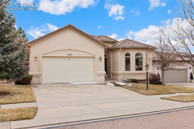 mediterranean / spanish-style home with a garage, a tiled roof, concrete driveway, and stucco siding