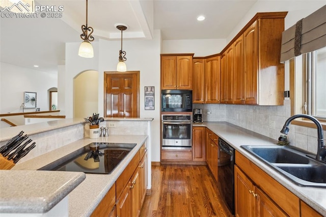 kitchen featuring decorative backsplash, dark wood-type flooring, hanging light fixtures, black appliances, and a sink