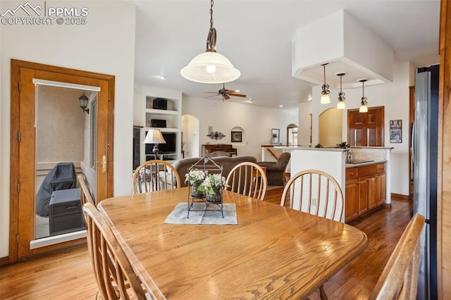 dining room with built in shelves, arched walkways, ceiling fan, light wood-type flooring, and baseboards