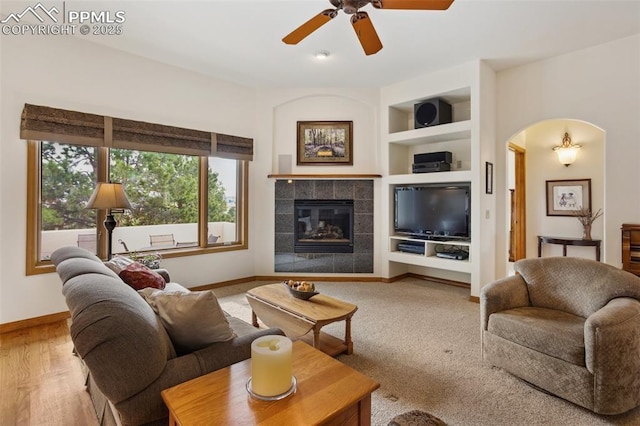 living room with built in features, arched walkways, a fireplace, and baseboards