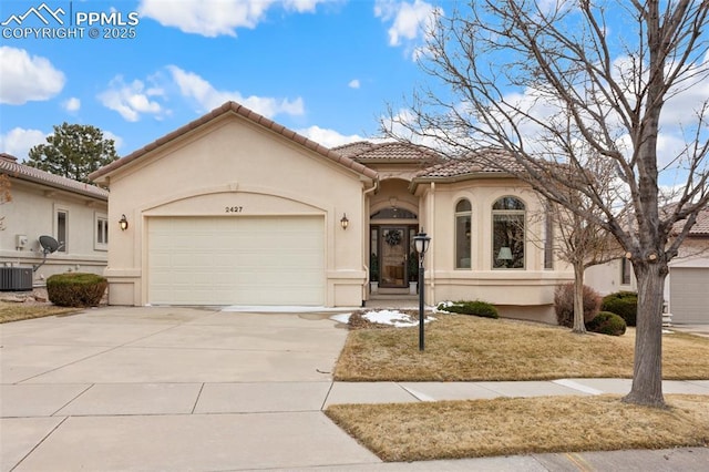 mediterranean / spanish house with central AC unit, an attached garage, a tiled roof, driveway, and stucco siding