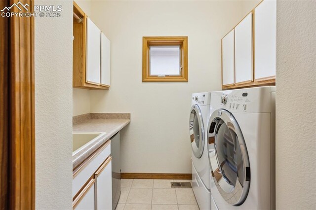 clothes washing area featuring light tile patterned floors, separate washer and dryer, cabinet space, and baseboards