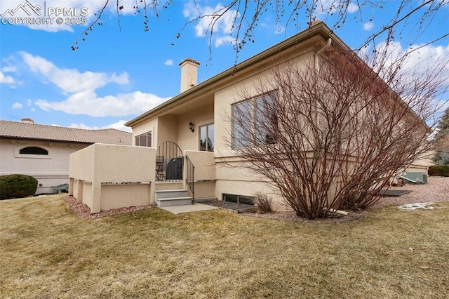 rear view of house with a lawn, a chimney, and stucco siding