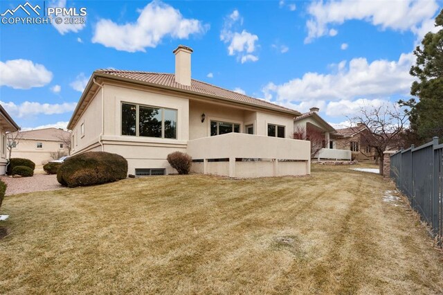 rear view of house featuring a chimney, a tiled roof, fence, a yard, and stucco siding