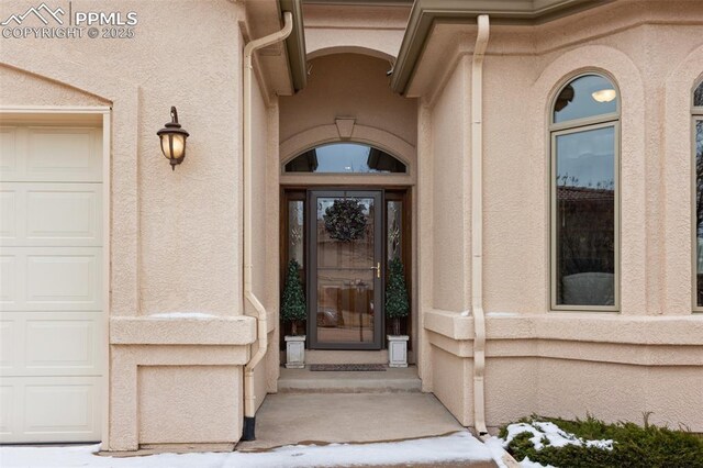 view of exterior entry with a garage and stucco siding