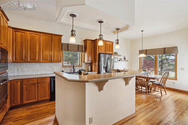 kitchen with tasteful backsplash, a raised ceiling, wood finished floors, and stainless steel fridge with ice dispenser