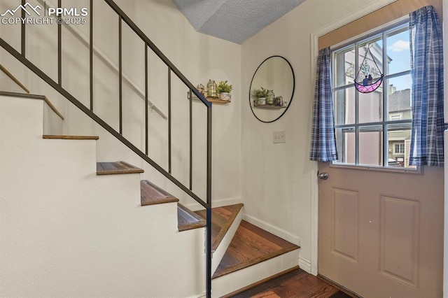 entrance foyer featuring a textured ceiling, stairs, dark wood-type flooring, and baseboards