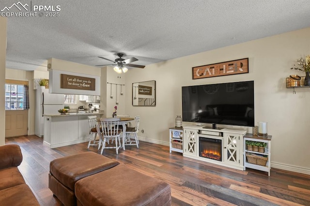 living area with a textured ceiling, wood finished floors, baseboards, and ceiling fan