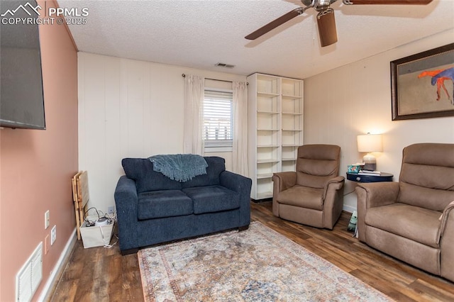 living area featuring visible vents, a textured ceiling, baseboards, and wood finished floors