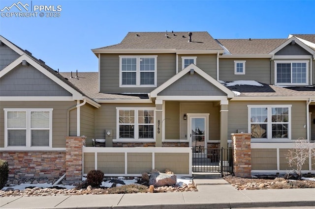 view of front of property featuring stone siding, a fenced front yard, and a shingled roof