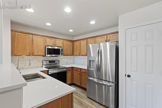 kitchen featuring light wood finished floors, tasteful backsplash, brown cabinets, stainless steel appliances, and a sink