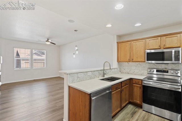 kitchen with stainless steel appliances, a sink, light countertops, light wood-type flooring, and decorative backsplash