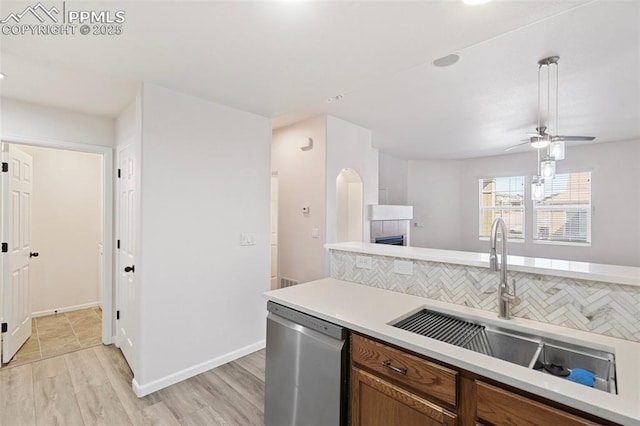 kitchen with light countertops, backsplash, stainless steel dishwasher, brown cabinetry, and a sink