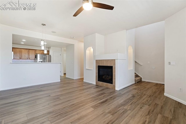 unfurnished living room with light wood-style floors, a ceiling fan, a fireplace, and stairs