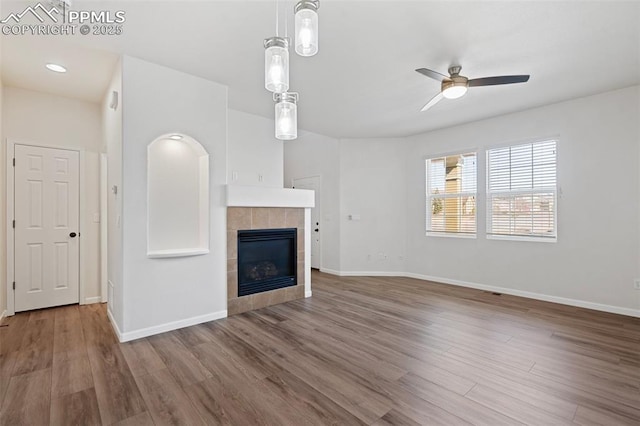 unfurnished living room with ceiling fan, a tiled fireplace, baseboards, and wood finished floors