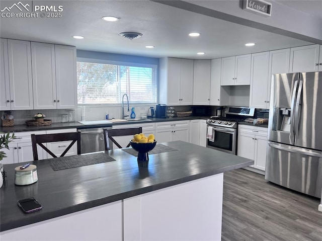 kitchen with visible vents, a sink, dark countertops, wood finished floors, and stainless steel appliances