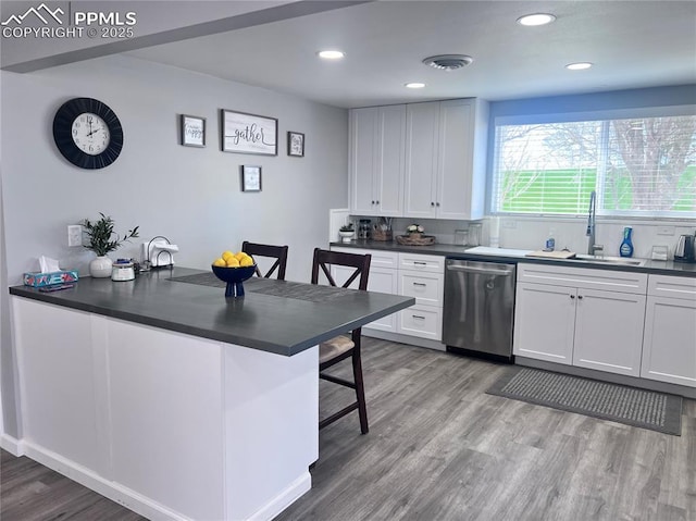 kitchen featuring visible vents, a sink, stainless steel dishwasher, dark countertops, and light wood-style floors