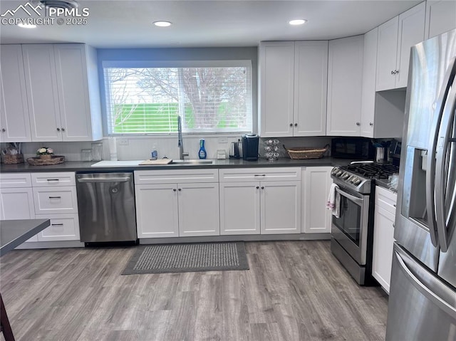 kitchen with light wood finished floors, white cabinetry, stainless steel appliances, and a sink