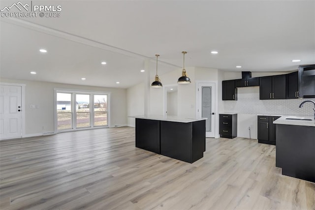 kitchen with a kitchen island, dark cabinets, lofted ceiling, light wood-style floors, and tasteful backsplash