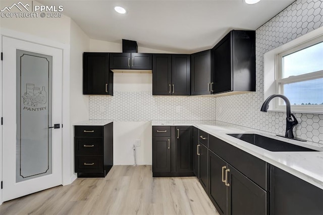 kitchen with tasteful backsplash, lofted ceiling, light wood-style flooring, dark cabinetry, and a sink