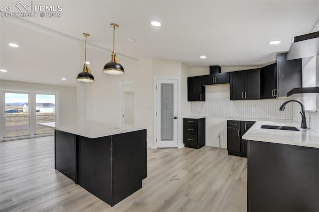 kitchen featuring light stone counters, a sink, decorative backsplash, light wood-style floors, and dark cabinets