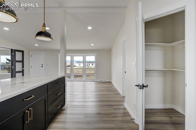 kitchen with dark cabinetry, light stone countertops, baseboards, recessed lighting, and light wood-type flooring