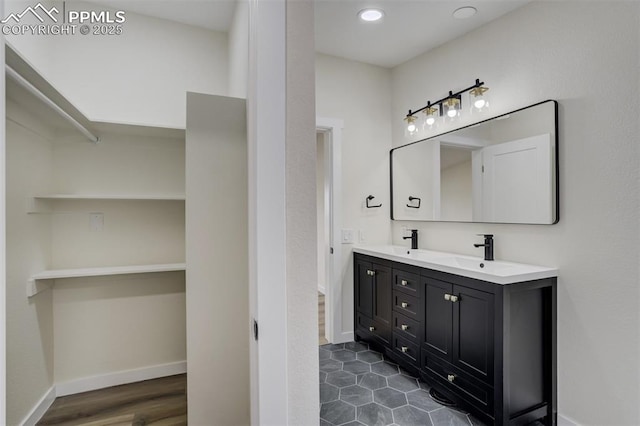 full bath featuring double vanity, a walk in closet, baseboards, and a sink