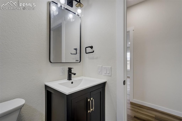 bathroom with toilet, vanity, baseboards, and wood finished floors