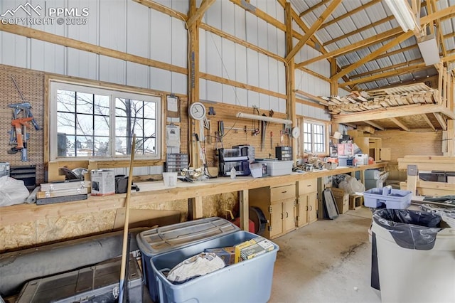 miscellaneous room featuring a workshop area, unfinished concrete flooring, metal wall, and high vaulted ceiling