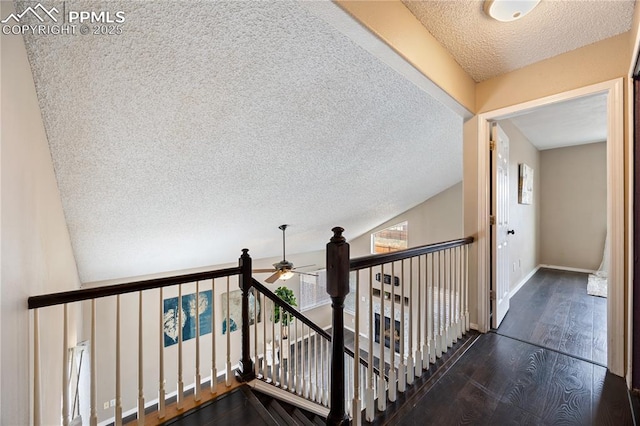 hall featuring a textured ceiling, wood finished floors, an upstairs landing, baseboards, and vaulted ceiling