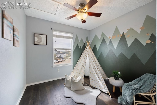 game room featuring a textured ceiling, an accent wall, baseboards, and dark wood-type flooring