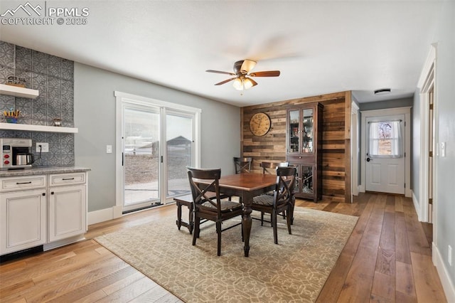 dining area featuring ceiling fan, light wood finished floors, wood walls, and baseboards