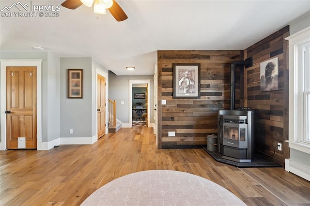 living area with light wood-type flooring, a wood stove, stairway, and baseboards