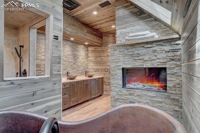 bathroom with an outdoor stone fireplace, double vanity, a freestanding tub, wood finished floors, and wooden ceiling