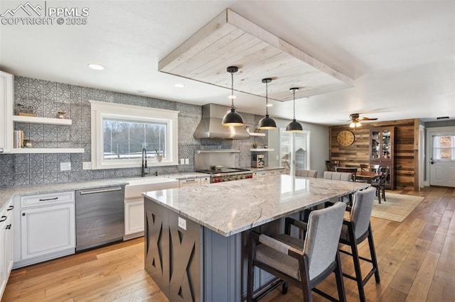 kitchen featuring wall chimney range hood, plenty of natural light, stainless steel appliances, and a sink