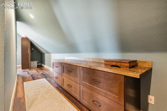 bonus room with baseboards, vaulted ceiling, dark wood-style flooring, and a textured wall