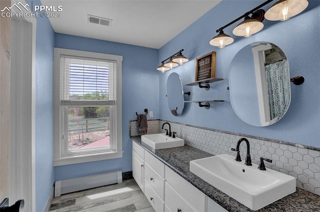 full bath with visible vents, a sink, baseboard heating, and wood finished floors