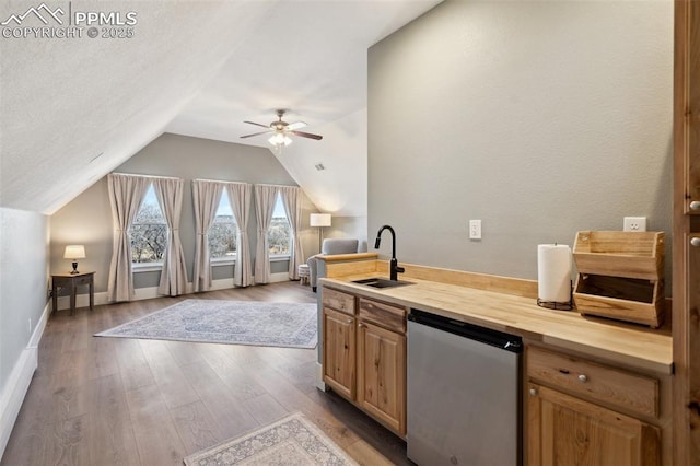 kitchen with dishwashing machine, butcher block counters, wood finished floors, vaulted ceiling, and a sink