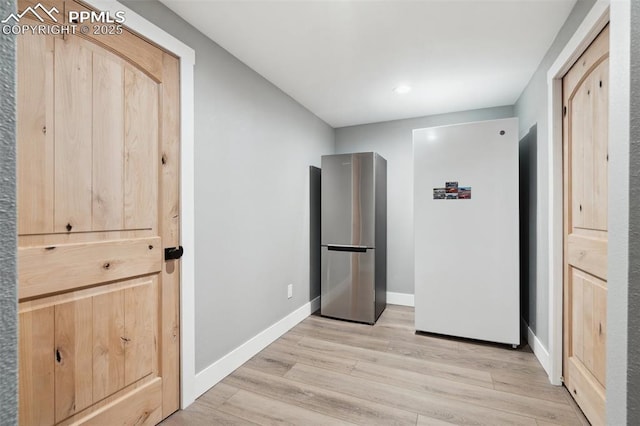 kitchen featuring light brown cabinetry, light wood-style flooring, freestanding refrigerator, and baseboards