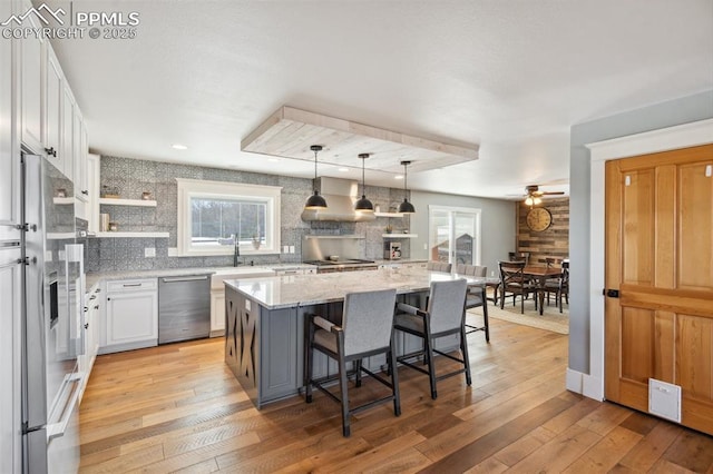 kitchen featuring stainless steel appliances, white cabinets, backsplash, light stone countertops, and light wood finished floors