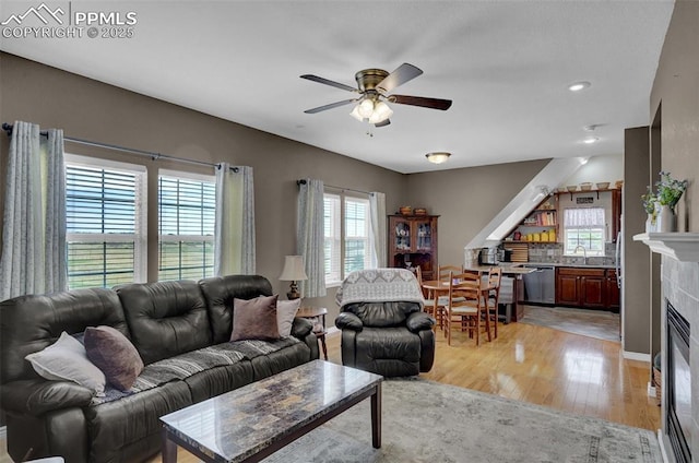 living room featuring ceiling fan, a glass covered fireplace, light wood-style flooring, and baseboards