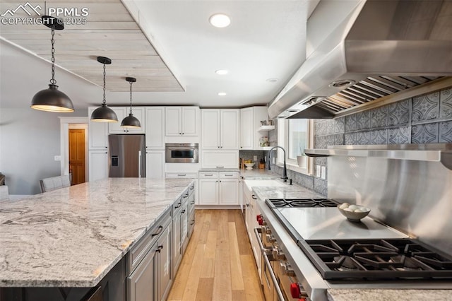 kitchen featuring light stone counters, stainless steel appliances, light wood-style flooring, white cabinets, and wall chimney range hood